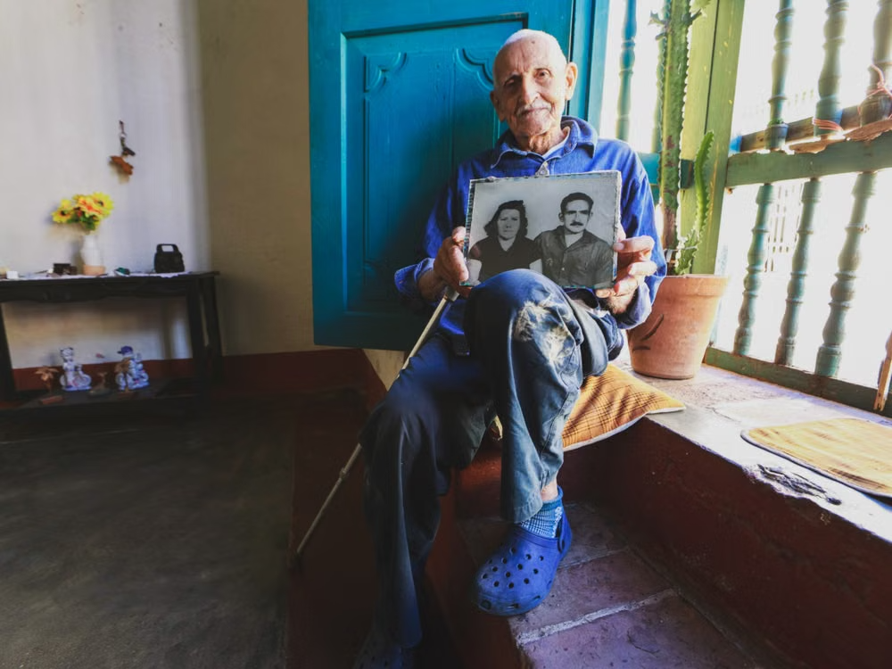 Hombre mayor sosteniendo una fotografía familiar durante una conversación sobre su historia de vida